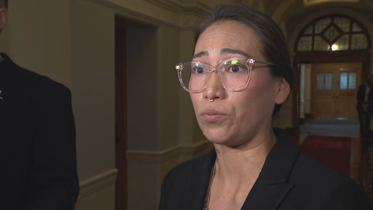 An Indigenous woman with glasses speaks to reporters.