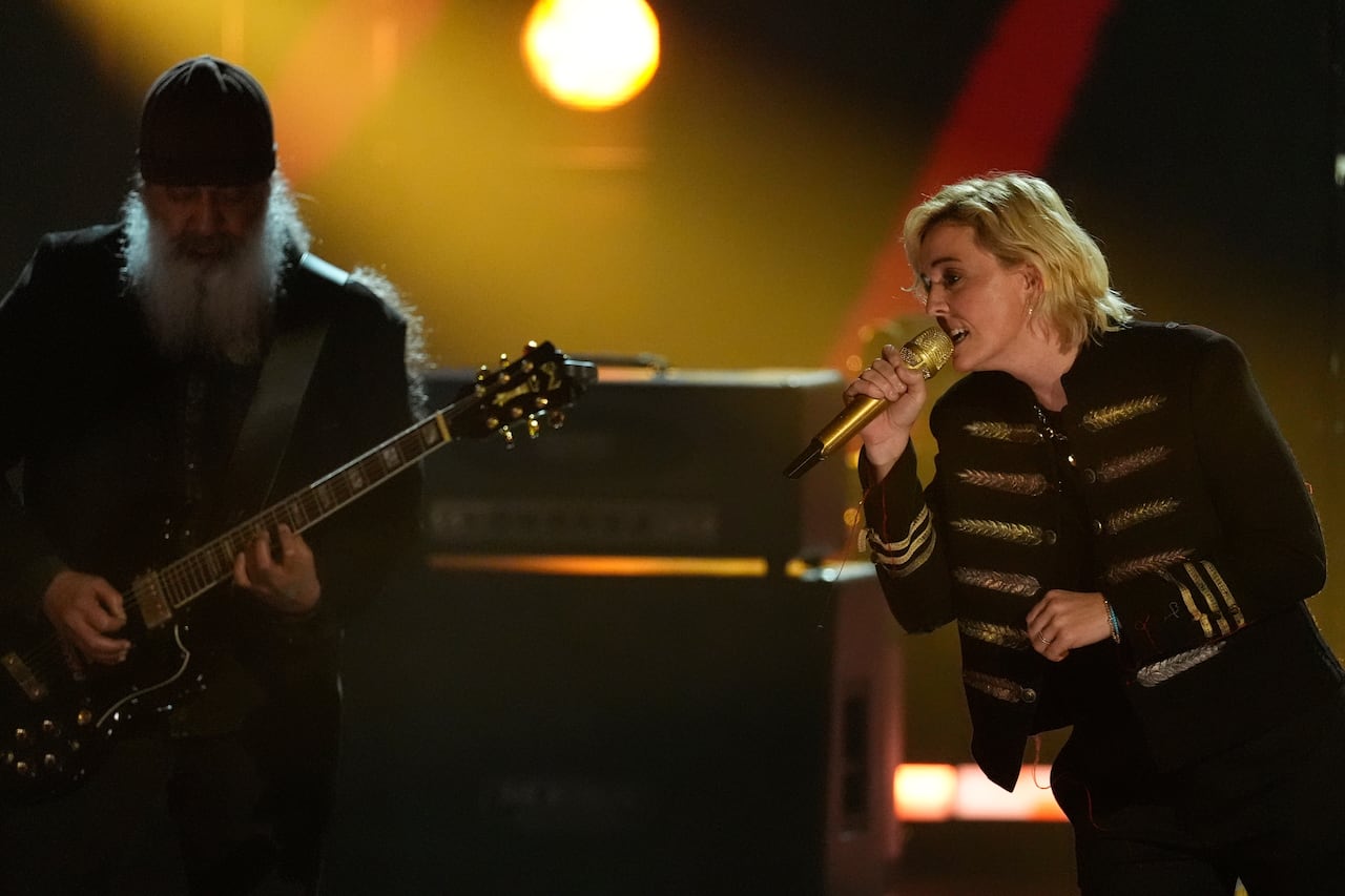 The man on the left plays the guitar, and the woman on the right leans towards him and sings into the microphone.