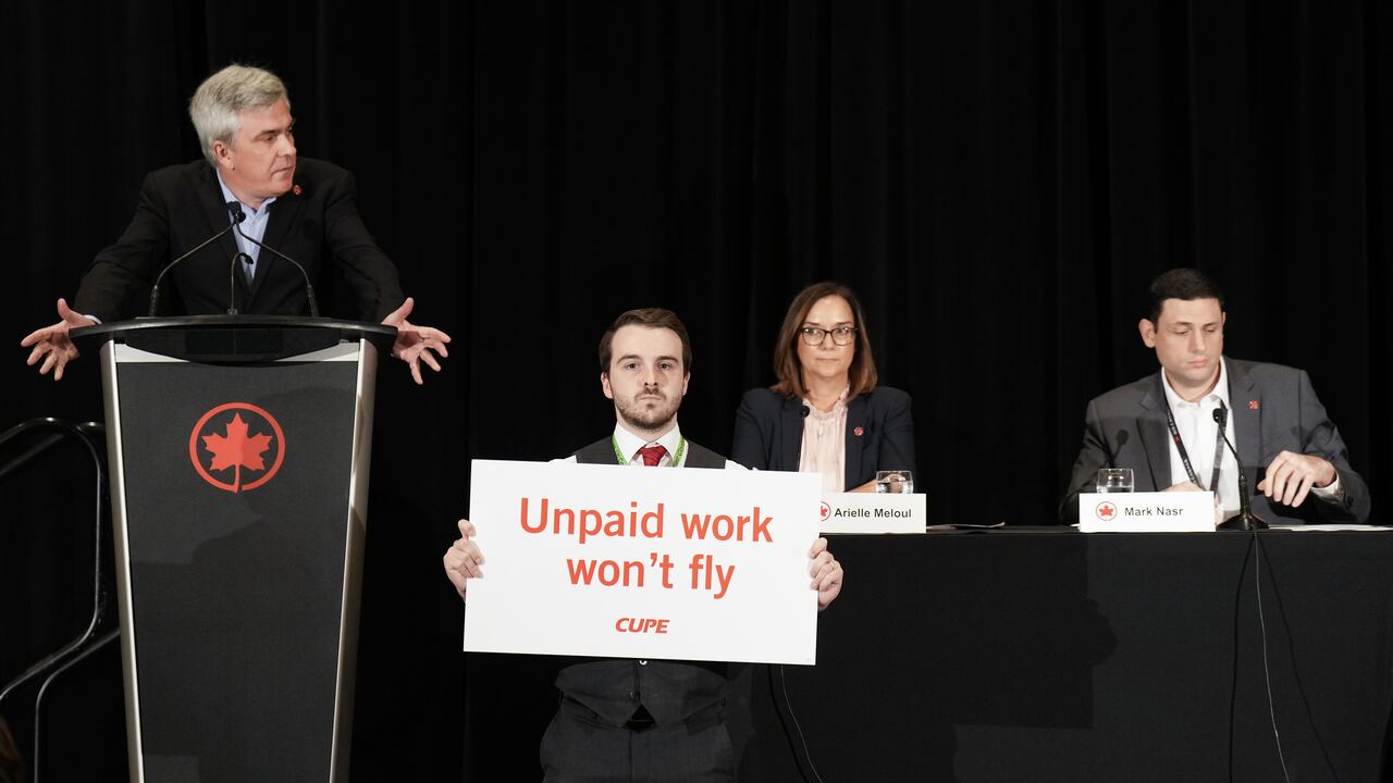 A man holds a sign reading "Unpaid work won't fly" during an Air Canada press conference.