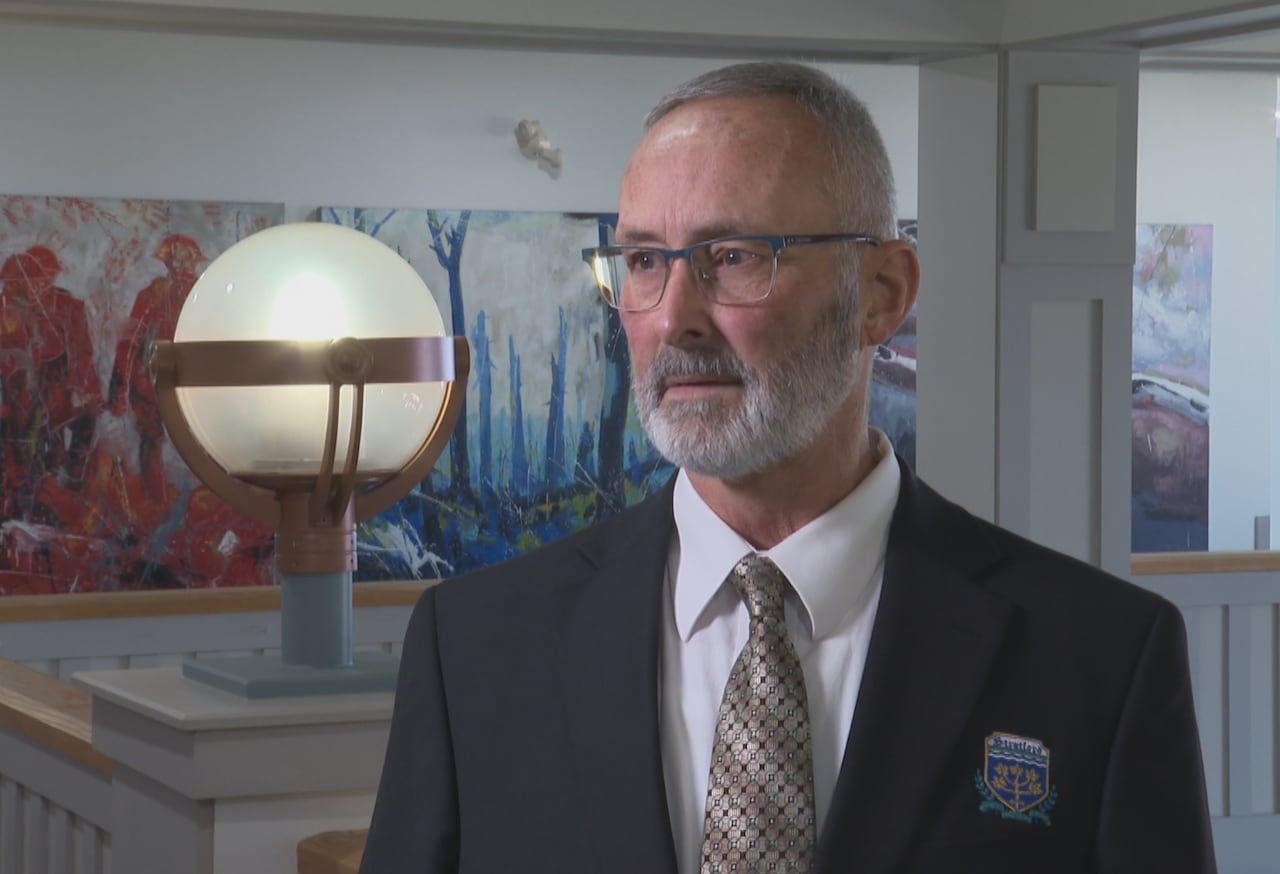 A man in a suit and tie standing indoors against a background with colorful abstract art