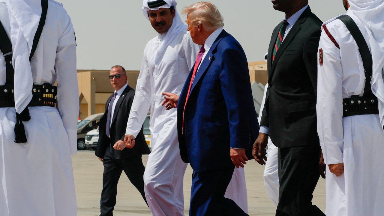 Two men speak on a red carpet at an airport.