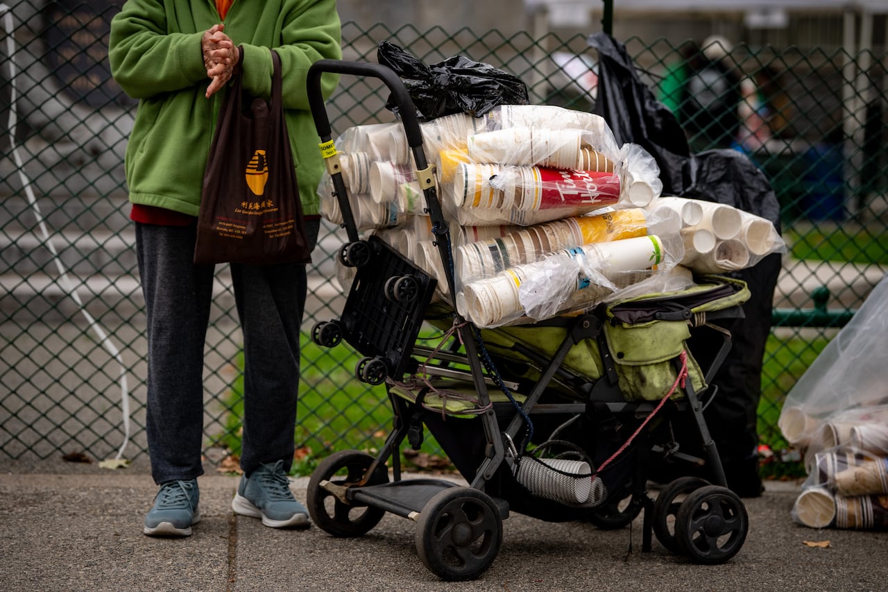 A woman stands with her hands together beside a cart with coffee cups stacked up in it.
