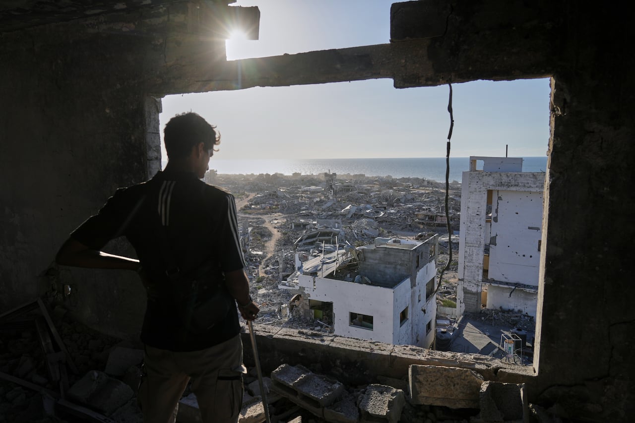 A man looks through a destroyed window overlooking a destroyed city as a ray of sun pokes through.