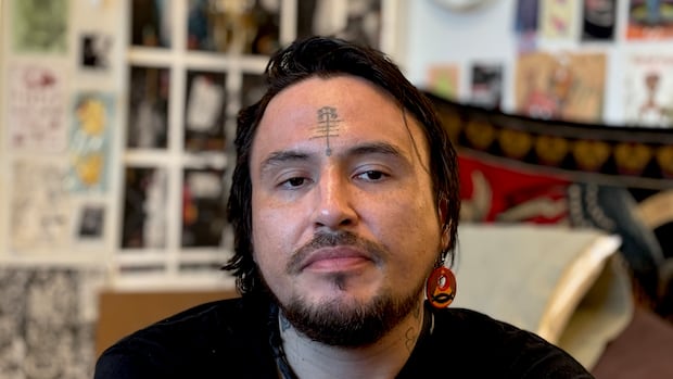 A person with dark hair and facial hair looks straight into the camera