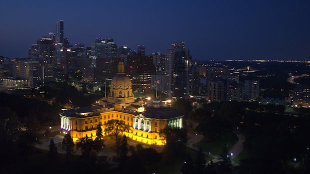 Alberta Legislature building and dome illuminated with Edmonton skyline in background at nightfall.