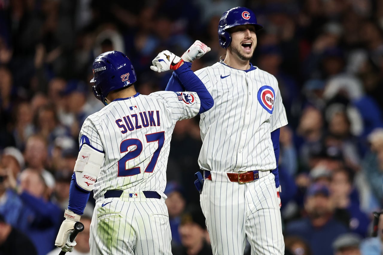 Two men's baseball player teammates, wearing white uniforms with red pinstripes, bump forearms in celebration.