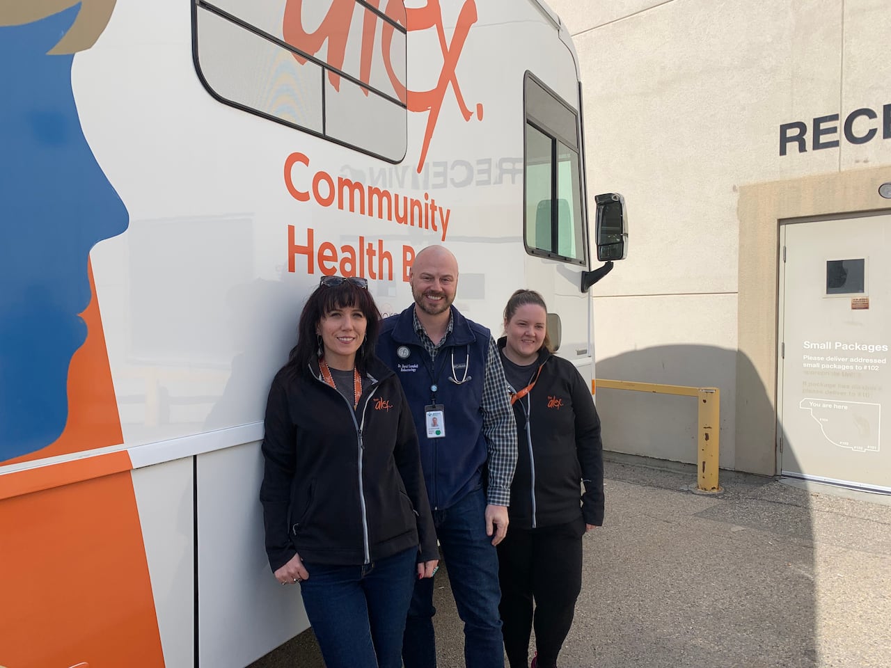 Two women and a man stand next to a large bus.