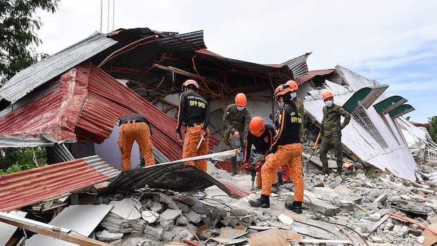 A group of people in orange helments and orange pants sift through rubble