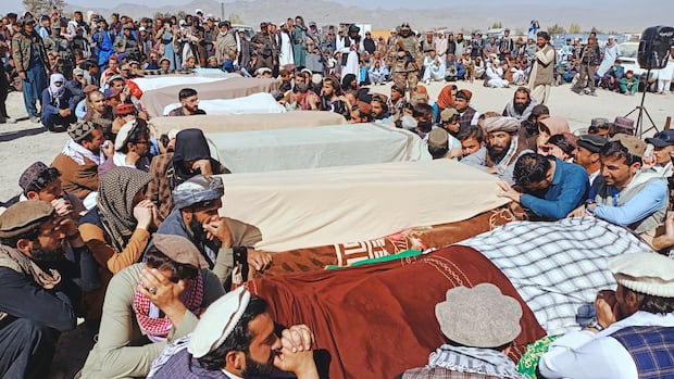 Mourners sit and gather around coffins in an outdoor ceremony.