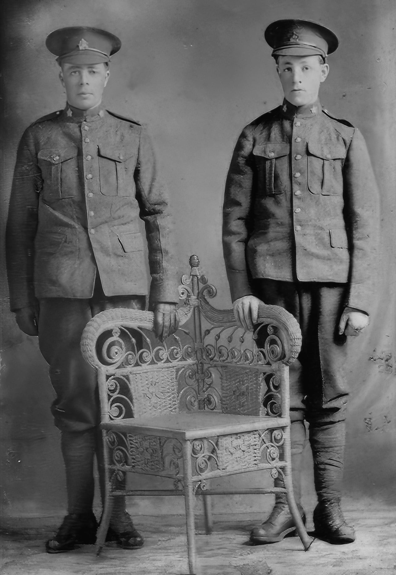 A black and white photo of two men in uniform standing with a chair between them.