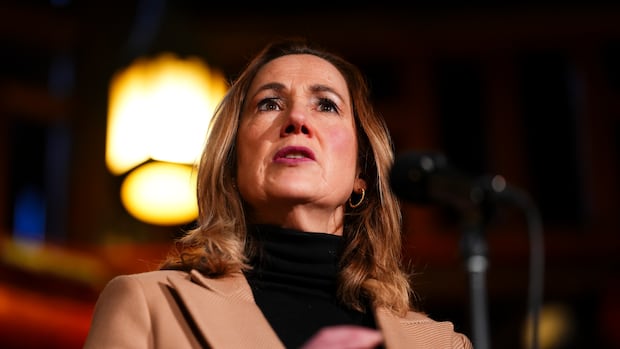 Woman speaking at microphone in black shirt with brown trench coat