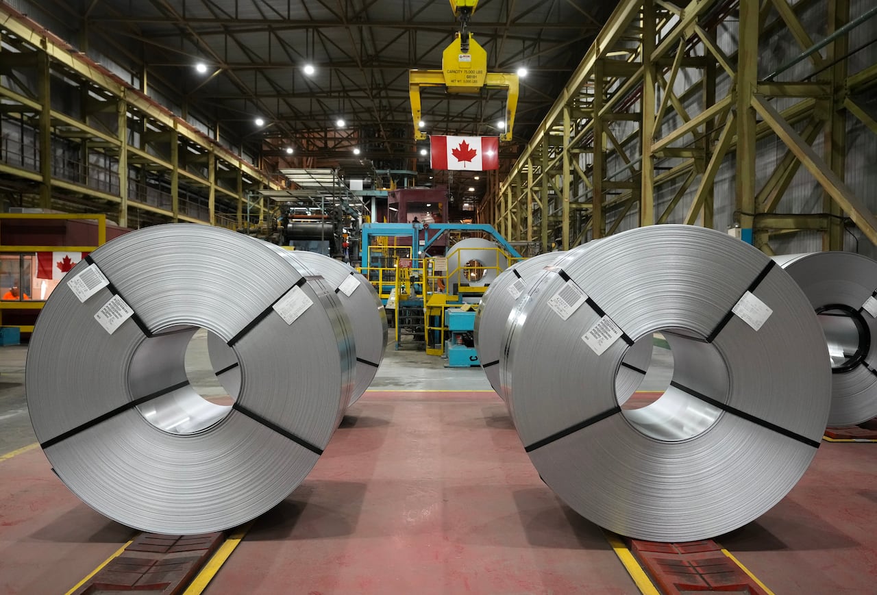 Los rollos de acero están alineados en una fábrica. Sobre ellos cuelga una bandera canadiense.