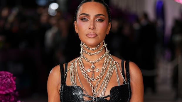 Kim Kardashian poses for photographers upon arrival at the premiere of the television series All's Fair on Wednesday, Oct. 22, 2025, in London.  A woman wearing many necklaces made of silver chain and with a crucifix pendant poses.