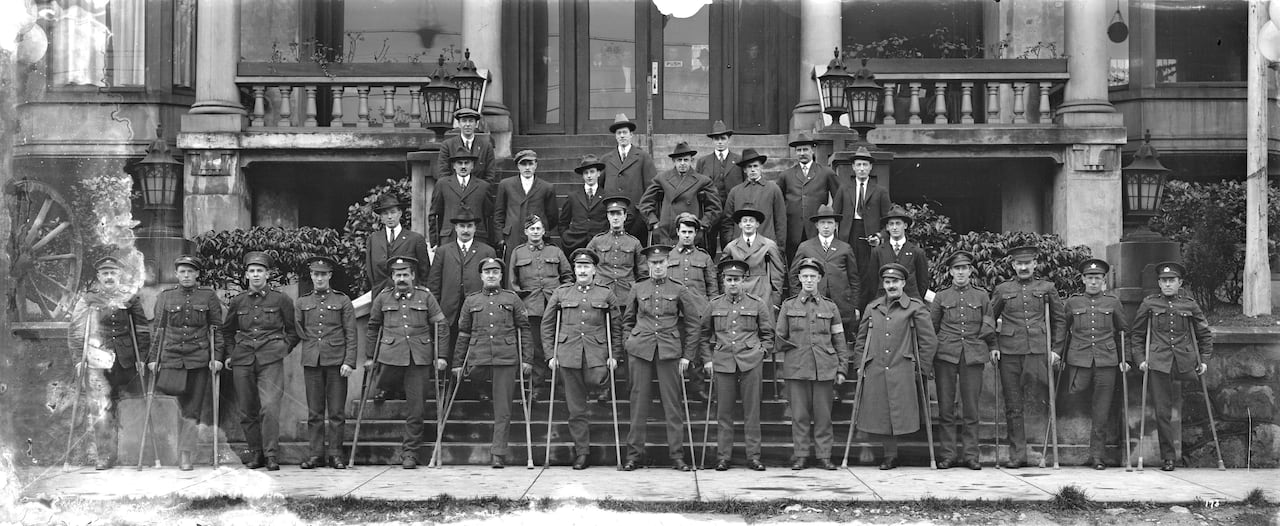 Black and white photo of dozens of men in military uniform, some with a missing leg, all holding crutches, lined up on stone steps in front of a building.
