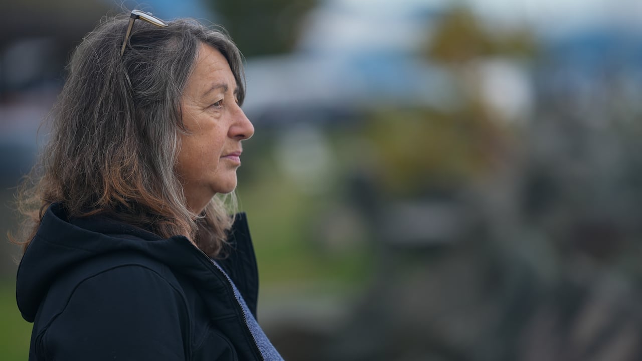 A side profile of a middle aged woman wearing a black jacket and looking into the distance.