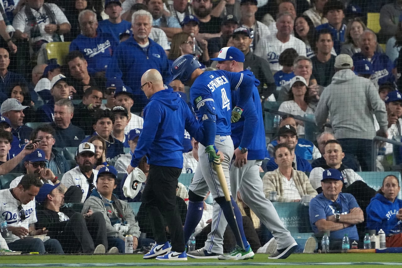 Baseball player is helped by team staff as he's walked off the diamond field injured.