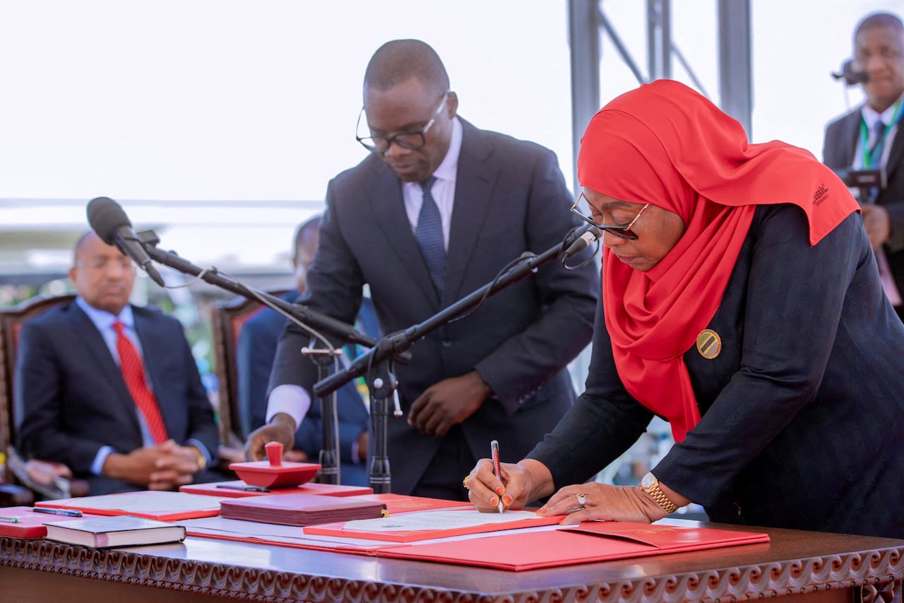 Newly elected Tanzanian president, dressed in a red hijab and black dress, signs her oath over a big oak table