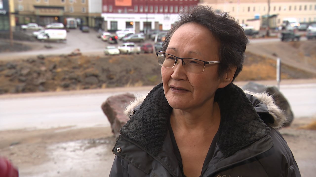 A woman stands on the side of the road, with a hotel parking lot in the background.