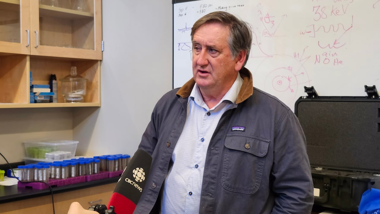 A man speaks into a CBC microphone. Behind him, a blackboard with formulas.
