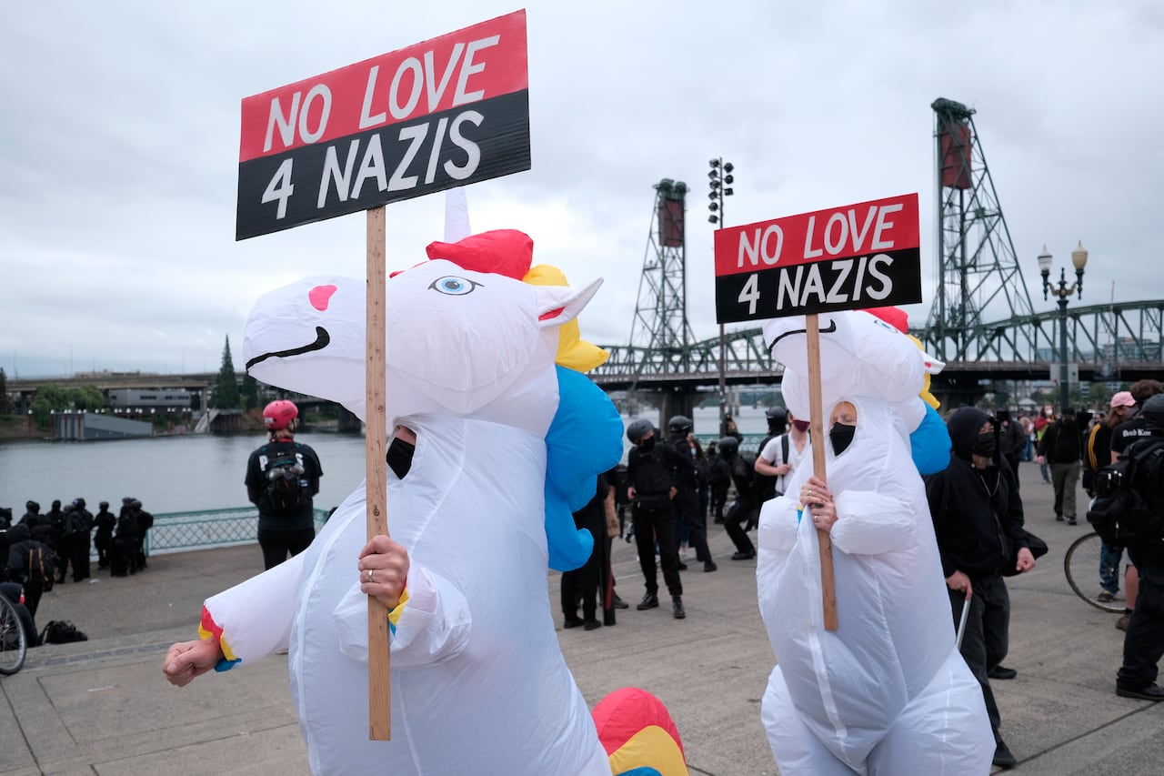 Two people dressed as unicorns catching the signs 'no love 4 Nazi' LOVE as Riot's burning gear police.