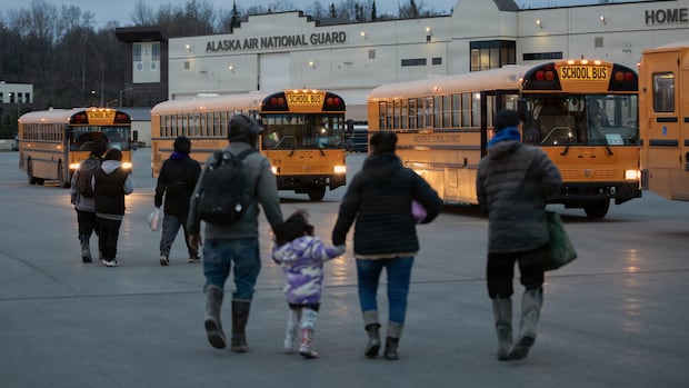 People walk across a lot toward a line of yellow school buses.