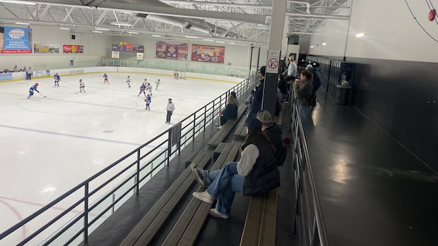 People in the stands are watching children play hockey. People are seen in the stands of an arena looking at children play hockey down below