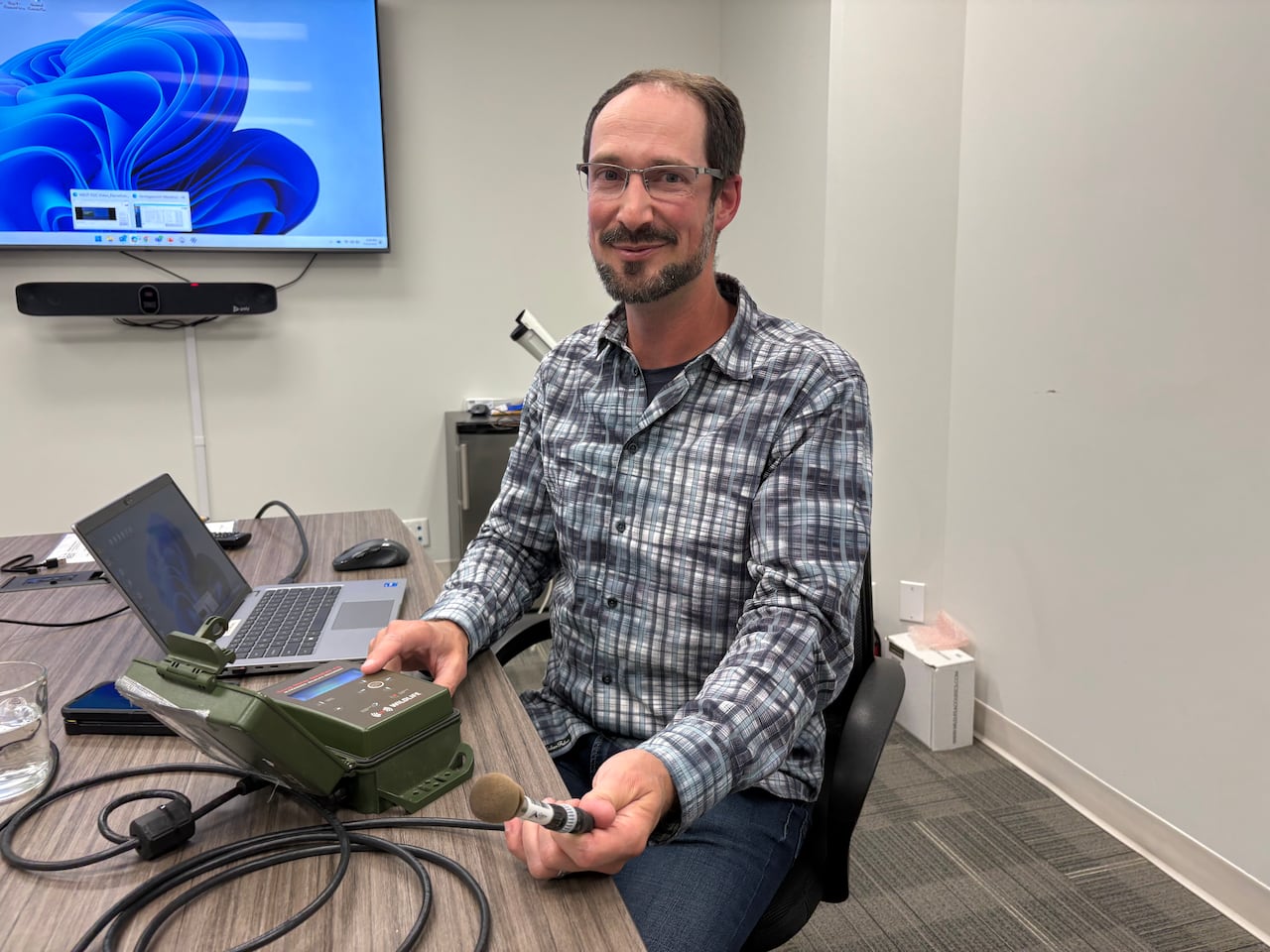 Um homem segura um equipamento de gravação enquanto está sentado à mesa.
