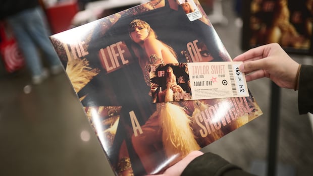 In a store setting, a pair of hands holds a vinyl copy of Taylor Swift's album Life of a Showgirl and a paper ticket overtop.