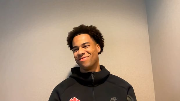 Tajon Buchanan Opens Up on Villarreal, Canada’s Rise & the Messi vs Ronaldo Debate Man smiles wearing a black shirt with red maple leaf
