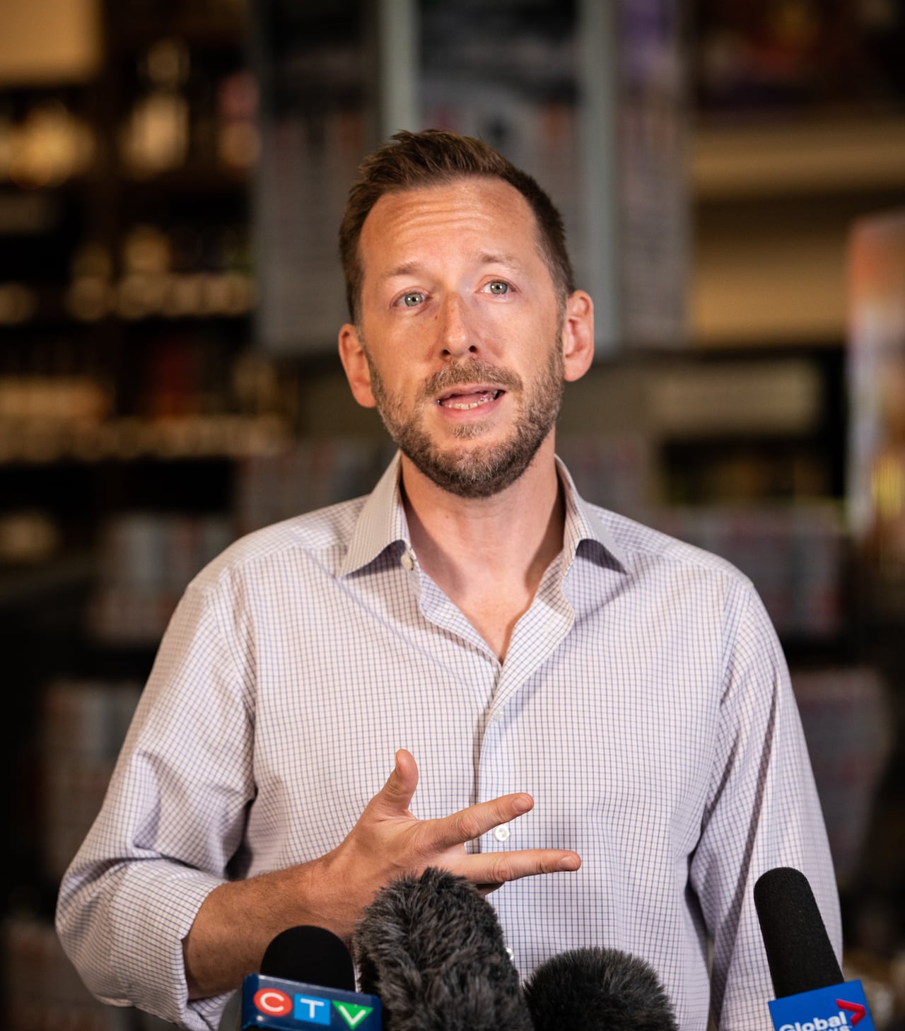 A bearded man speaks to a gaggle of mics in a liquor store.