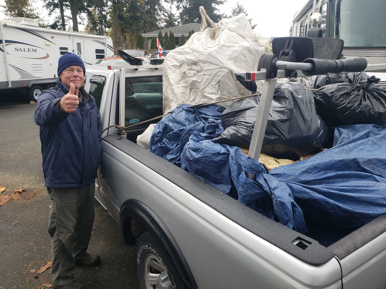 A man giving a thumbs-up stands next to a pickup truck filled with debris. 