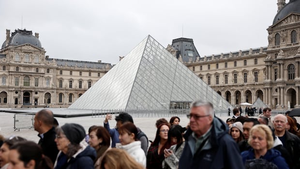 Tourists walk near the glass Pyramid of the Louvre Museum, in Paris, France. 