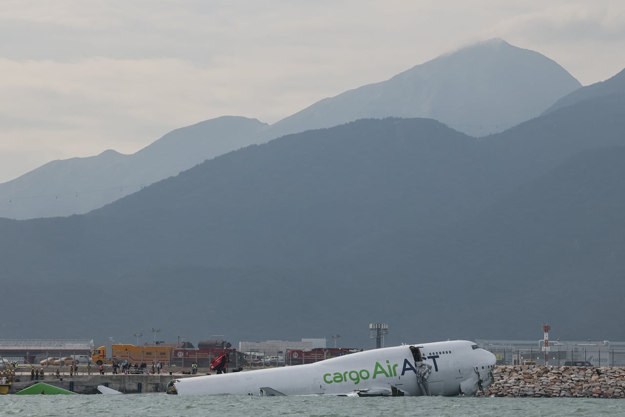 The broken fuselage of a cargo jet lies half submerged in water.