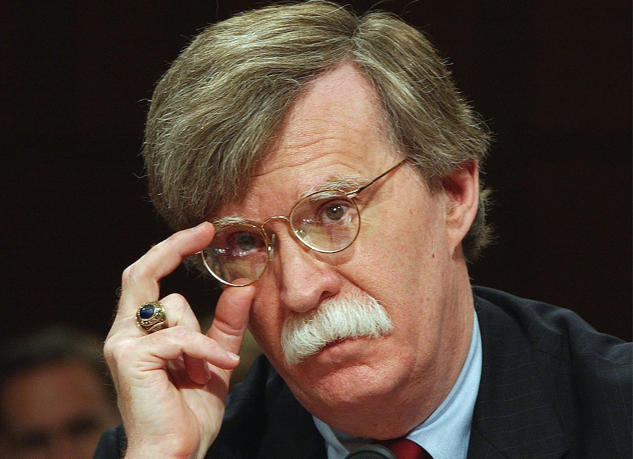 Close-up of a man sitting to the side, adjusting his glasses.
