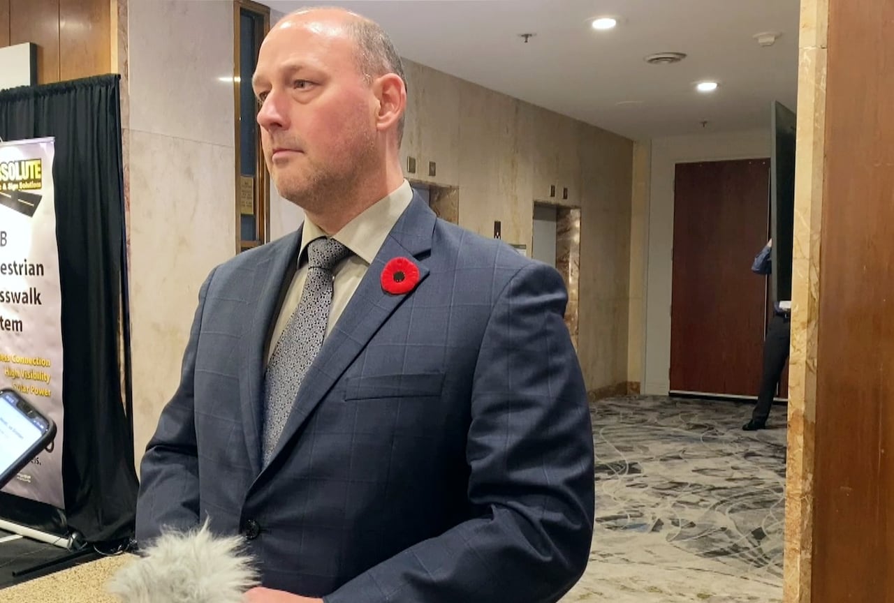 A bald achromatic antheral successful a navy suit and reddish poppy connected his thorax stands successful a edifice hallway