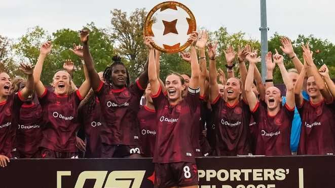 A female soccer team hoists a trophy while smiling in celebration.