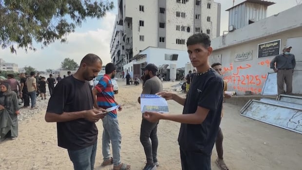 Two men holding papers and looking at the camera. Building in the background. 
