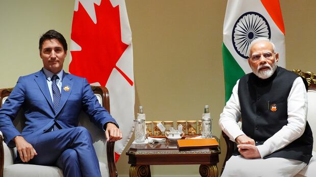 A man in a suit and a man in a traditional Indian dress sit for a photo with a table in between.