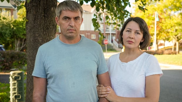 A man and woman link arms and stand in front of a yard.