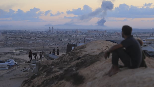 A man sits as destruction looms in the background.