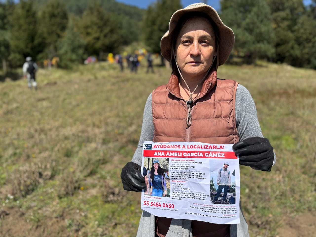 A woman with a hat holds the missing poster for her daughter in front of her.