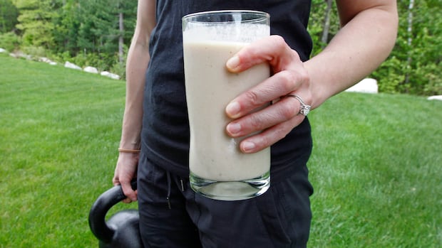 In this image taken on Tuesday, May 15, 2012, Amanda Perry holds a protein shake for lunch and a kettleball as she poses at her home in Tyngsborough, Mass. Perry, a gym owner and personal trainer, blends a vegan protein powder with almond milk, natural peanut butter, ice and a banana as a drink in her daily diet. A surge in protein as both a nutrient and a marketing element has been added to the American diet. (AP Photo/Charles Krupa) A woman's hand holding a glass with a protein shake with a kettlebell in her other hand.