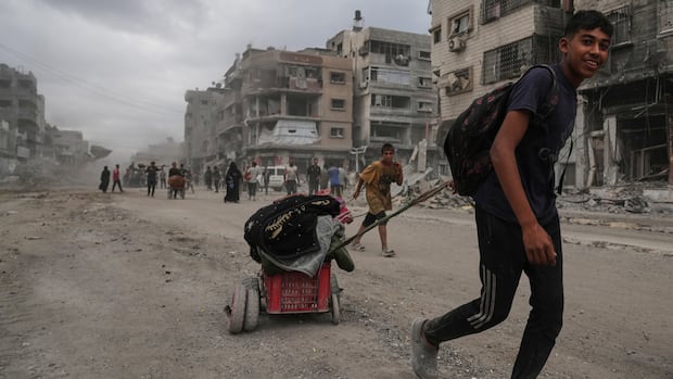 A teenager drags his belongings up a street in ruins. 