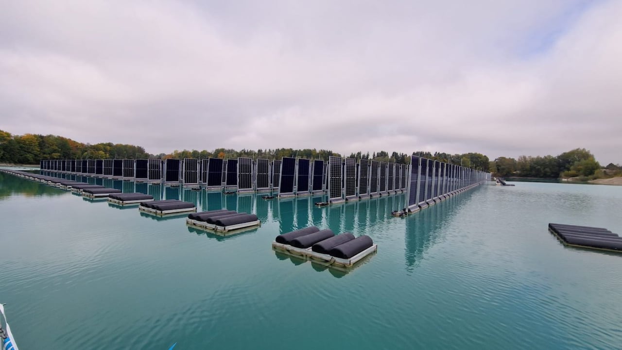 Floating solar panels mounted vertically in rows on a lake surrounded by floating pallets of black cylinders