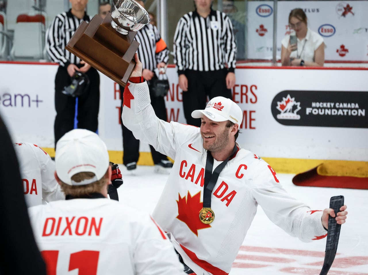 A male Para hockey player representing Canada smiles while holding up a trophy with his right hand as a gold medal hangs around his neck.