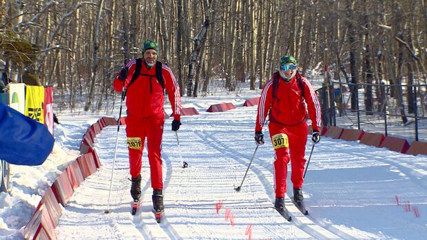 Two cross-country skiiers, dressed in red, race to the Canadian Birkebeiner finish line. Two cross-country skiiers, dressed in red, cross the finish line at the Canadian Birkebeiner.