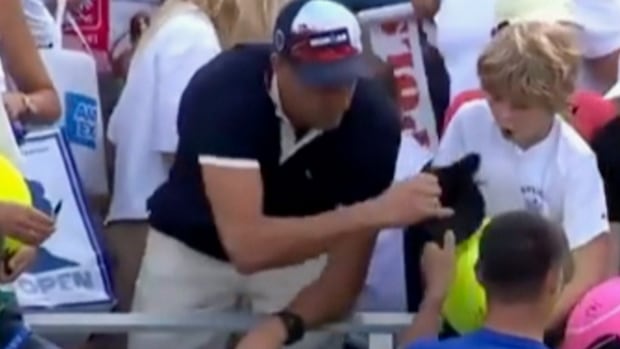 A picture of a video of a man who takes a hat from a boy at a tennis court.