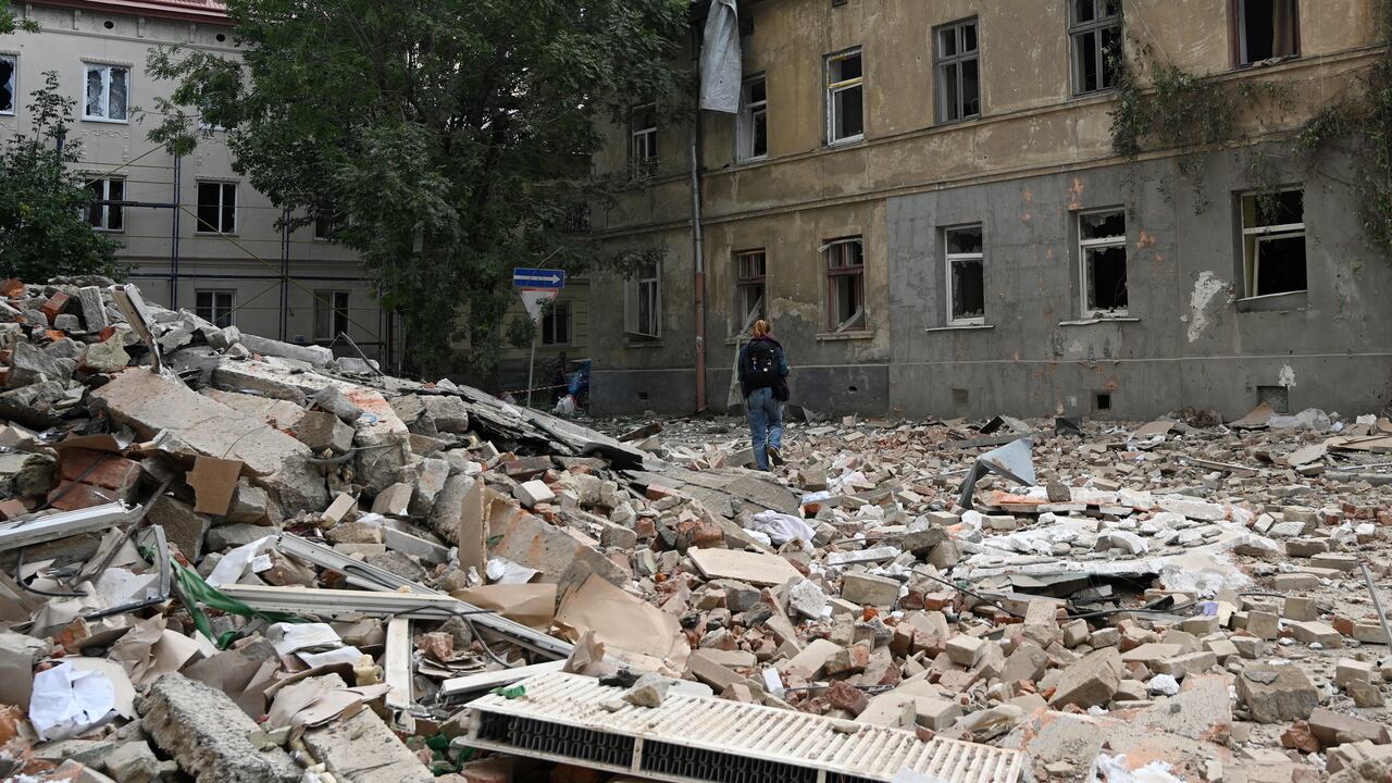 A person walks past a damaged residential building with nearby rubble.