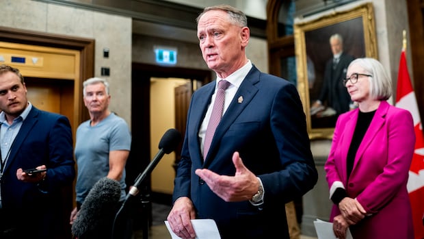 Man stands in small group of people at door of House of Commons speaking at microphone