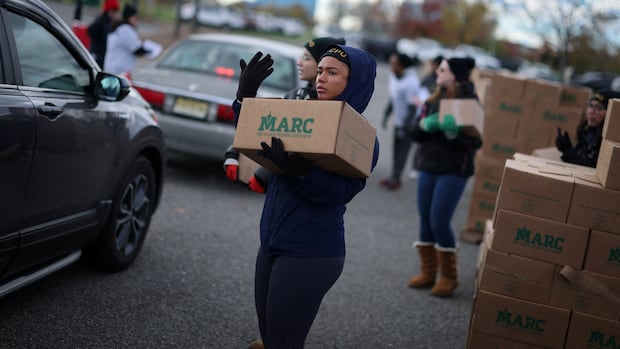 Volunteers load boxes of food into cars during an event held by the Community FoodBank of New Jersey in partnership with Bergen County to deliver emergency food relief to Federal workers and SNAP recipients amid the U.S. government shutdown in Leonia, New Jersey, U.S., November 6, 2025. REUTERS/Mike Segar TPX IMAGES OF THE DAY A woman wearing a hooded jacket holds a box while standing next to a vehicle in what appears to be parking lot. Other people stand near her in the background.